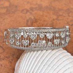 Estate 14KT white gold filigree pave diamond hearts hinged bangle cuff bracelet. Pave diamonds go half way around, back side is patterned with cut-out diamond shapes, however, without diamonds. Length: 7" Width: 18mm Weight: 21.8g Tapered back Double safety clasp 1.00 CT TW diamond; SI clarity; G-H color Excellent estate condition Shown with other bracelets which are sold separately Gold Filigree, Hinged Bangle, Diamond Heart, Pave Diamonds, Diamond Shapes, Cuff Bracelet, Cut Out, Bangles, Diamonds