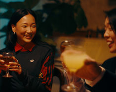 two women are holding wine glasses and smiling at each other as they sit in a restaurant