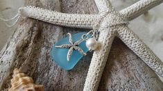 a starfish charm with a pearl and sea glass pendant on a piece of driftwood