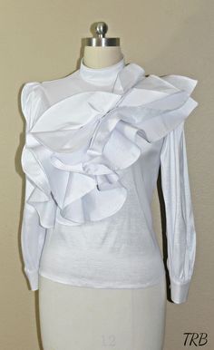 Add a high fashion statement to your wardrobe with this tiered asymmetrical ruffled Blouse. If you love being unique and the center of attention, this blouse will defiantly have all eyes on you! The low cut turtleneck neckline adds a soft, feminine touch and others will defiantly be impressed with your fashion sense. The cascade of asymmetrical ruffles across the front gives the blouse a unique wow factor. The blouse has a tailor fit and is very comfortable to wear. Made of 100% Taffeta, light w Elegant High Neck Top With Ruffles, Elegant High Neck Ruffle Top, Chic Fitted Blouse With Ruffles, Chic Fitted Ruffle Blouse, Elegant Party Tops With Ruffles, Elegant Ruffled Tops For Party, Elegant Evening Tops With Ruffle Hem, Elegant Evening Top With Ruffle Hem, Elegant Ruffle Hem Top For Evening