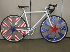 a white bicycle with red, white and blue spokes is parked in front of a wall