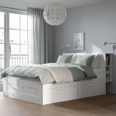 a white bed with two drawers underneath it and a window in the backround