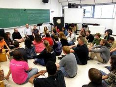 a group of people sitting on the floor in front of a blackboard