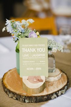 a wooden slice with a card on it and flowers in a jar sitting on top of it