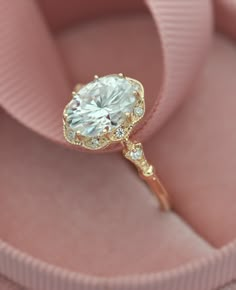 a close up of a diamond ring in a pink velvet box with ribbon around it