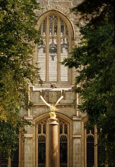 an old building with a clock on it's side and trees surrounding it in the foreground