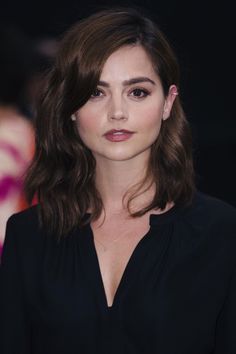 a woman with shoulder length brown hair wearing a black shirt and posing for the camera