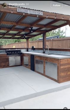 an outdoor kitchen with stainless steel appliances under a pergolated roof that reads, welcome to our porch