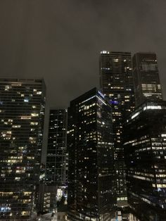 some very tall buildings at night time with lights on in the windows and dark clouds