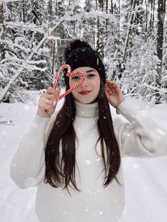 a woman holding up a candy cane in front of her face while standing in the snow