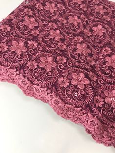 a close up of a pink lace on a white table cloth with flowers and leaves