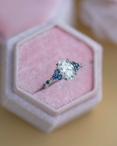 an engagement ring with blue and white stones on it sitting in a pink velvet box