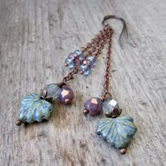 a pair of earrings with leaves and beads hanging from them on a wooden surface,