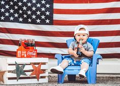 a baby sitting in a blue chair next to an american flag and some soda bottles