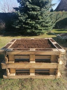 a wooden pallet filled with dirt in the grass next to a tree and fence