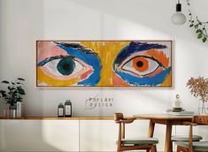 an abstract painting hangs on the wall above a dining room table with chairs and a potted plant