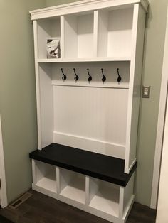 a white and black bench with some hooks on it's back wall in a room