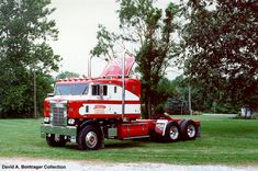 a red and white semi truck parked in the grass