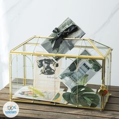 a glass house with plants inside on a wooden table next to a card holder and envelope