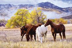 three horses are standing in the grass with mountains in the background