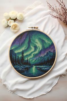 a cross - stitch aurora bore is shown on a white cloth next to some flowers