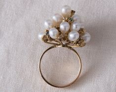 "This over the top, eye catching cocktail ring has to be worn to be appreciated. The ring features a cluster of 17 lustrous white pearls, accented by yellow gold nuggets and genuine gemstones arranged through out the design. The setting sits high on top of the finger but the band is flat and comfortable to wear. This retro era ring truly embodies the \"big and bold\" look of that time period and will definitely be a conversation starter on your hand! GEMSTONES: Genuine Sapphires: 2 @ 1.75mm, Gen White Cluster Ring With 17 Jewels, Unique White Pearl Ring For Formal Occasions, Fine Jewelry Pearl Ring With 17 Jewels For Wedding, Heirloom Multi-stone Pearl Ring For Wedding, Unique Cluster Jewelry For Formal Occasions, Formal White Multi-stone Pearl Ring, Heirloom Multi-stone Pearl Wedding Ring, Fine Jewelry Pearl Cluster Ring For Wedding, Cluster Pearl Wedding Ring