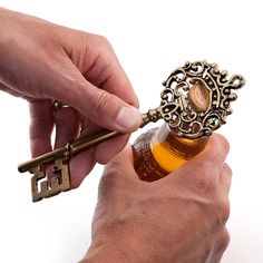 a person holding a bottle opener with a key in it's mouth and another hand opening the bottle