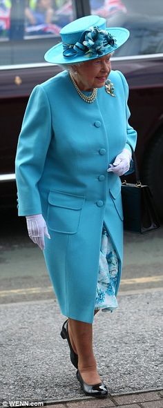 the queen is walking down the street wearing a bright blue coat and matching hat with white gloves