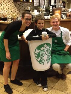 three people in green aprons are holding a starbucks cup and posing for the camera