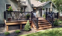 a wooden deck with black iron railings and steps leading up to the front door