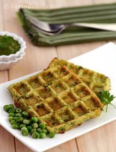 two waffles on a white plate with peas and green sauce in the background