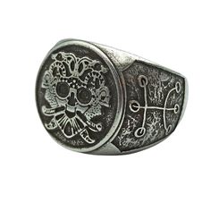 a silver ring with a skull and cross design on the front, sitting on top of a white surface