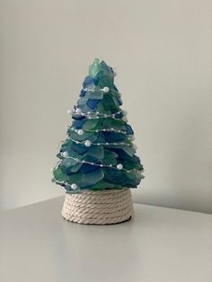 a small christmas tree made out of glass beads and rope on a white table top