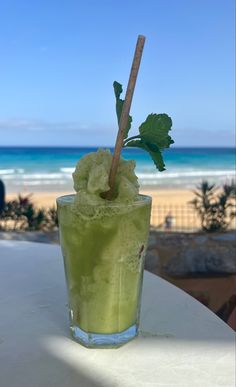 a green drink sitting on top of a white table next to the ocean with a wooden stick sticking out of it