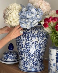 two hands reaching for flowers in a blue and white vase