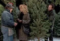 two men and a woman standing in front of a christmas tree stand talking to each other