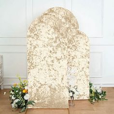 a white and gold wedding arch with flowers on the floor next to it, in front of a wall