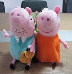 two peppa pig stuffed animals sitting next to each other on a wooden table with chairs in the background