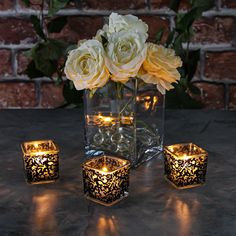 three lit candles are sitting on a table next to some flowers and glass vases