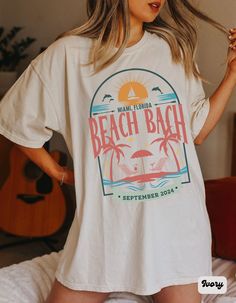 a woman standing on top of a bed wearing a t - shirt that says beach bach