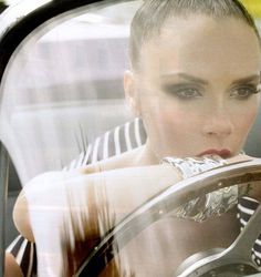 a woman sitting in a car with her hand on the steering wheel and looking at the camera