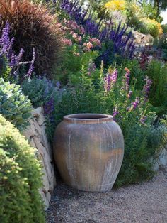 a large vase sitting in the middle of a garden filled with purple and yellow flowers