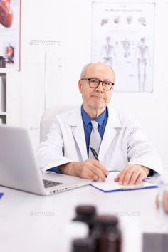 a male doctor sitting at his desk in front of a laptop computer - stock photo - images