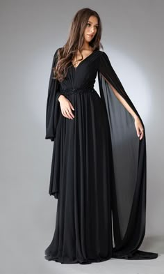 Here's a long formal dress with dramatic flair. With draped long sleeves that flow behind like a double train, this long dance dress is an exotic choice for prom, galas, and other black-tie events. In misses and some plus sizes, this stylish long evening gown has a gathered v-neck bodice with a deep v-back and a sparkly empire waist that tops the free-flowing floor-length a-line skirt. Priced under $200, this bohemian-style long formal dress balances chic style and affordability to perfection. Black Evening Dress Elegant, Modest Chic, Gown With Cape, Chiffon Embroidery, Dama Dresses, Long Cape, Long Formal Dress, Mother Wedding Dress, Fitted Wedding Dress