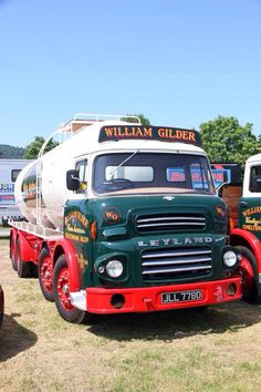 two green and red trucks parked next to each other on a grass covered field with trees in the background