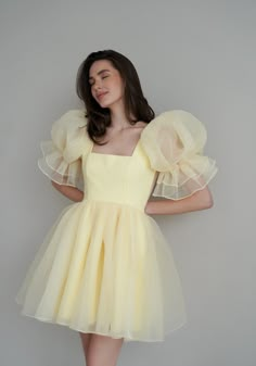 Introducing the Britney Dress in a delightful light yellow: a stunning creation crafted from delicate bubble organza. This lightweight dress features an elegant silhouette with a voluminous floating skirt that moves gracefully with every step. The charming puff sleeves add a whimsical touch, making it perfect for any special occasion. The Britney Dress is enclosed with delicate bow ties down the back, adding a romantic and feminine detail that completes the look. In light yellow, this dress exud Princess Dress For Women, Puff Sleeve Tulle Dress, Dresses With Transparent Sleeves, Gown Yellow, Bat Mitzvah Dresses Modest, Dress With Short Sleeves Formal, Flimsy Dress, Georgette Short Dress, Yellow Dress Design