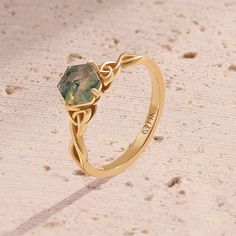 a gold ring with a green stone in the center on top of sand and dirt