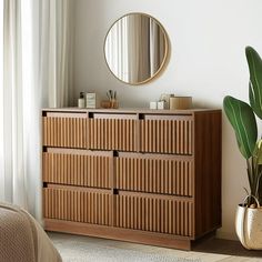 a bedroom with a bed, mirror and plant in the corner on the sideboard