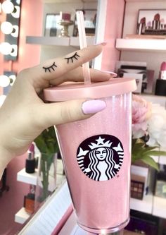 a woman's hand holding up a pink starbucks cup with eyelashes on the side