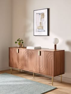 a wooden sideboard in a living room next to a rug and framed painting on the wall